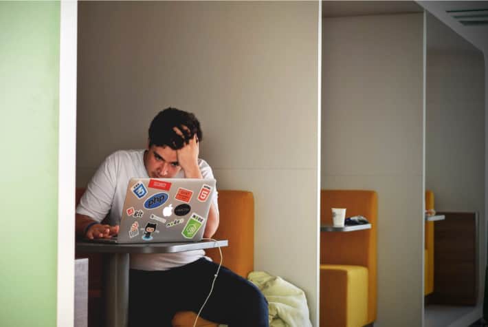 Mann sitzt in einer Nische und blickt angestrengt an seinen Laptop