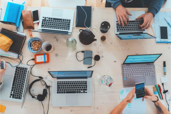 Mehrere Personen arbeiten an einem Schreibtisch an Laptops und Smartphones